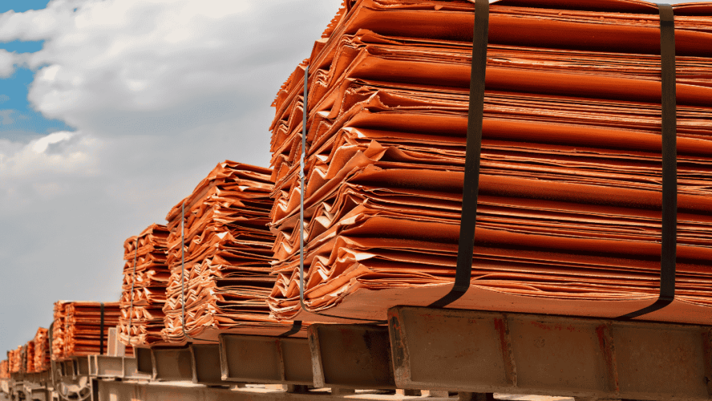 Stacks of copper cathodes bundled on pallets awaiting export, under a partly clouded sky.