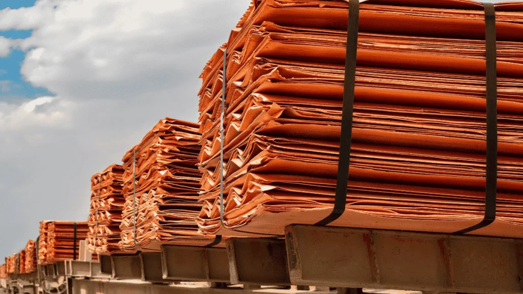 Stacks of copper cathodes bundled on pallets awaiting export, under a partly clouded sky.