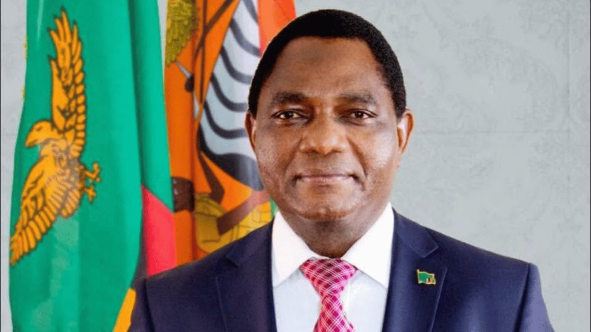 Official portrait of Zambian President Hakainde Hichilema against the national flag and coat of arms