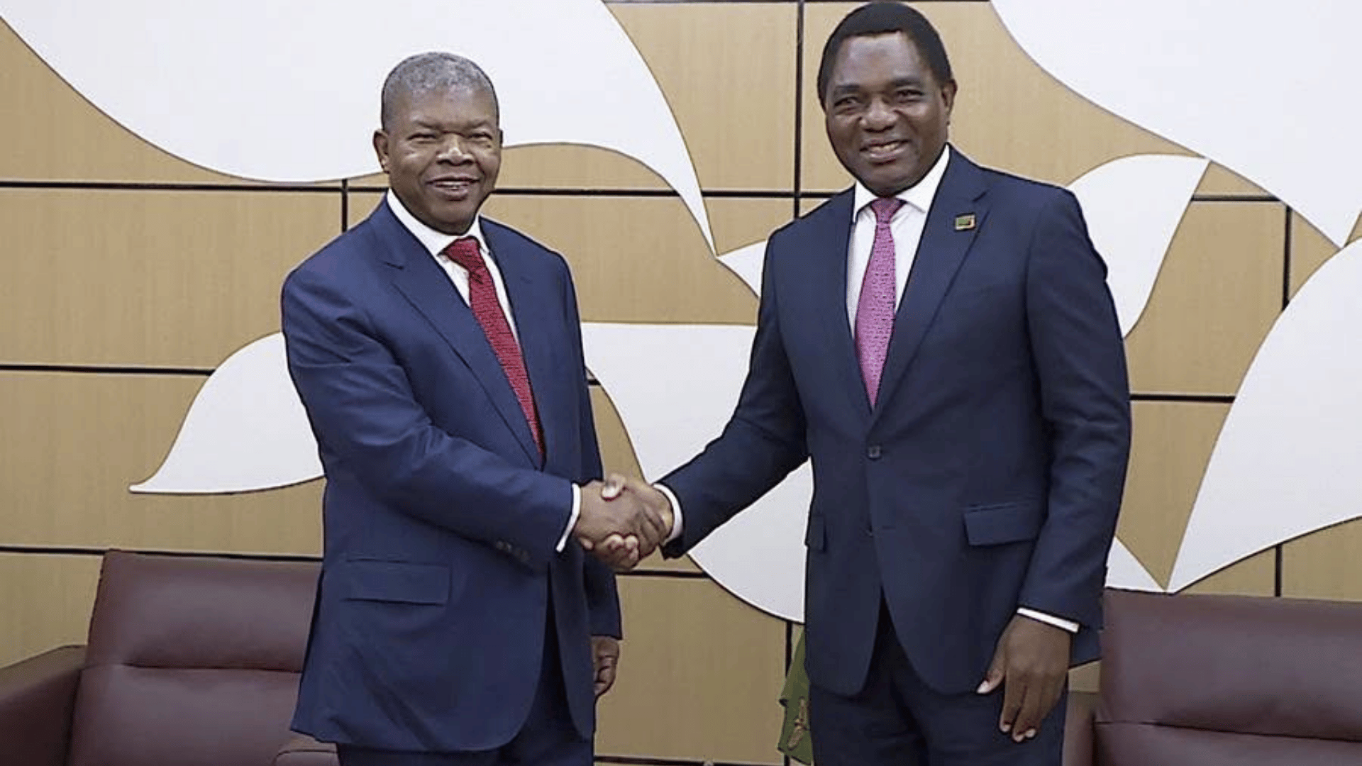 Zambia's President Hakainde Hichilema and Angola's President João Lourenço shake hands in a formal meeting room