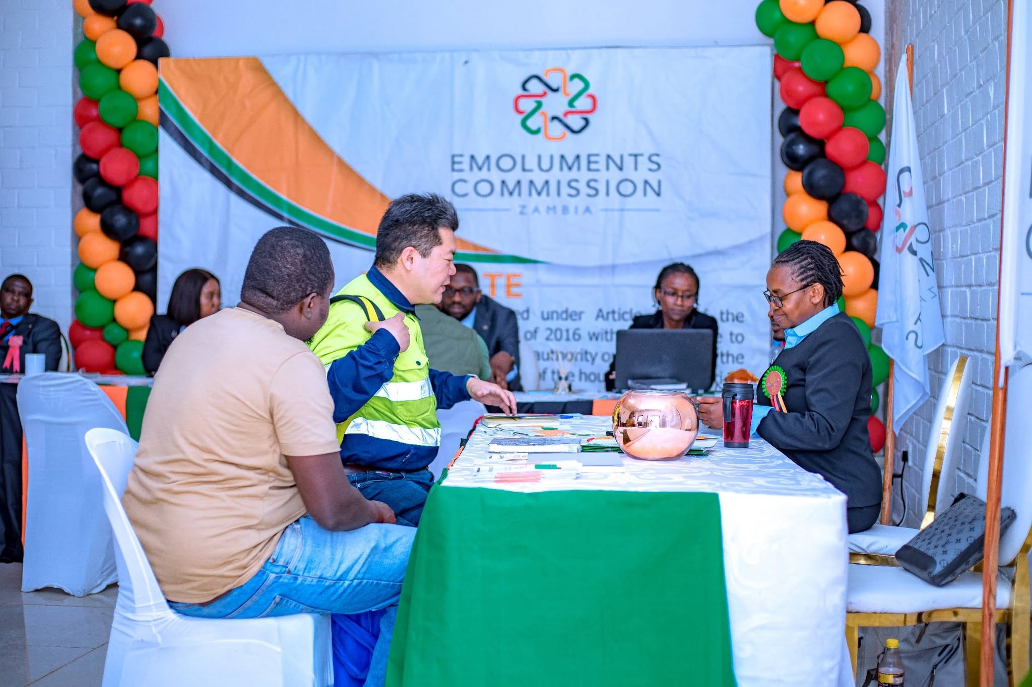 Visitors engaging with staff at the Emoluments Commission stand in Zambia Hall