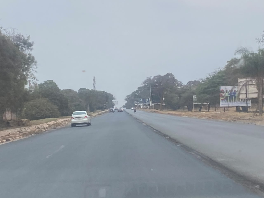 Light early-morning traffic travelling along a broad Lusaka road under a pale, hazy sky.