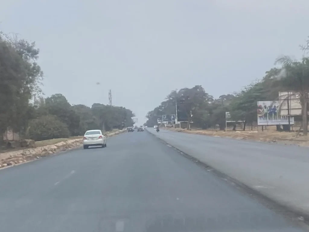 Light early-morning traffic travelling along a broad Lusaka road under a pale, hazy sky.