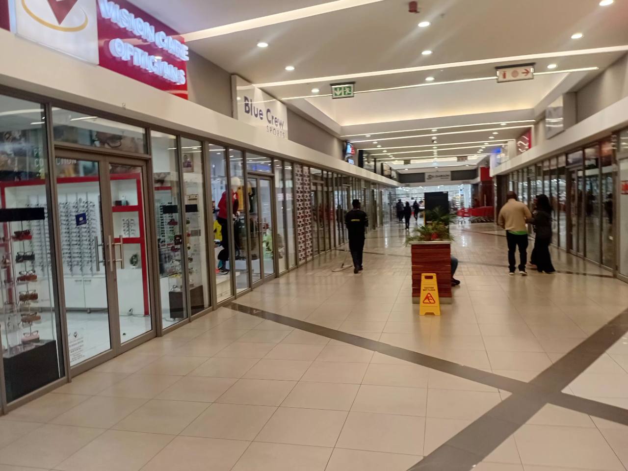 Vision Care Opticians, Blue Crew Sports and shoppers along an interior passage at Novare Pinnacle Mall