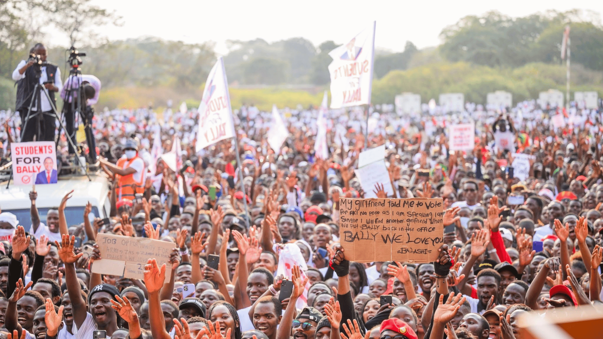 A large crowd of students holding signs and raising their hands at State House in Lusaka