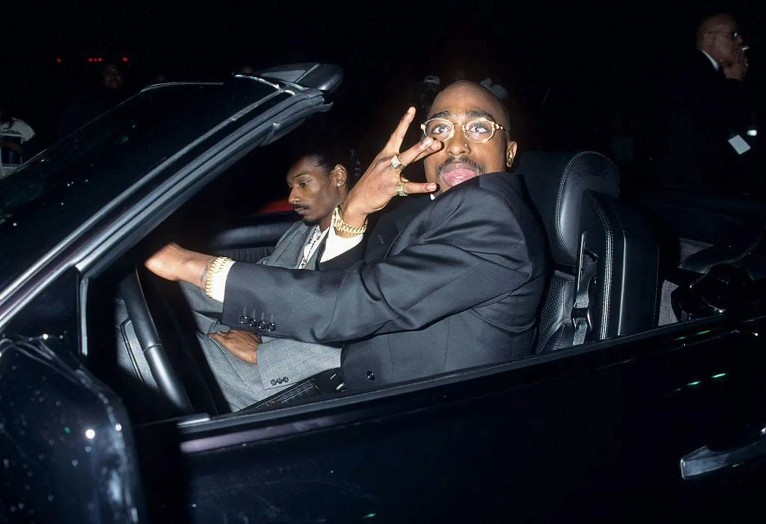 Tupac Shakur seated beside music executive Suge Knight in a car at night.