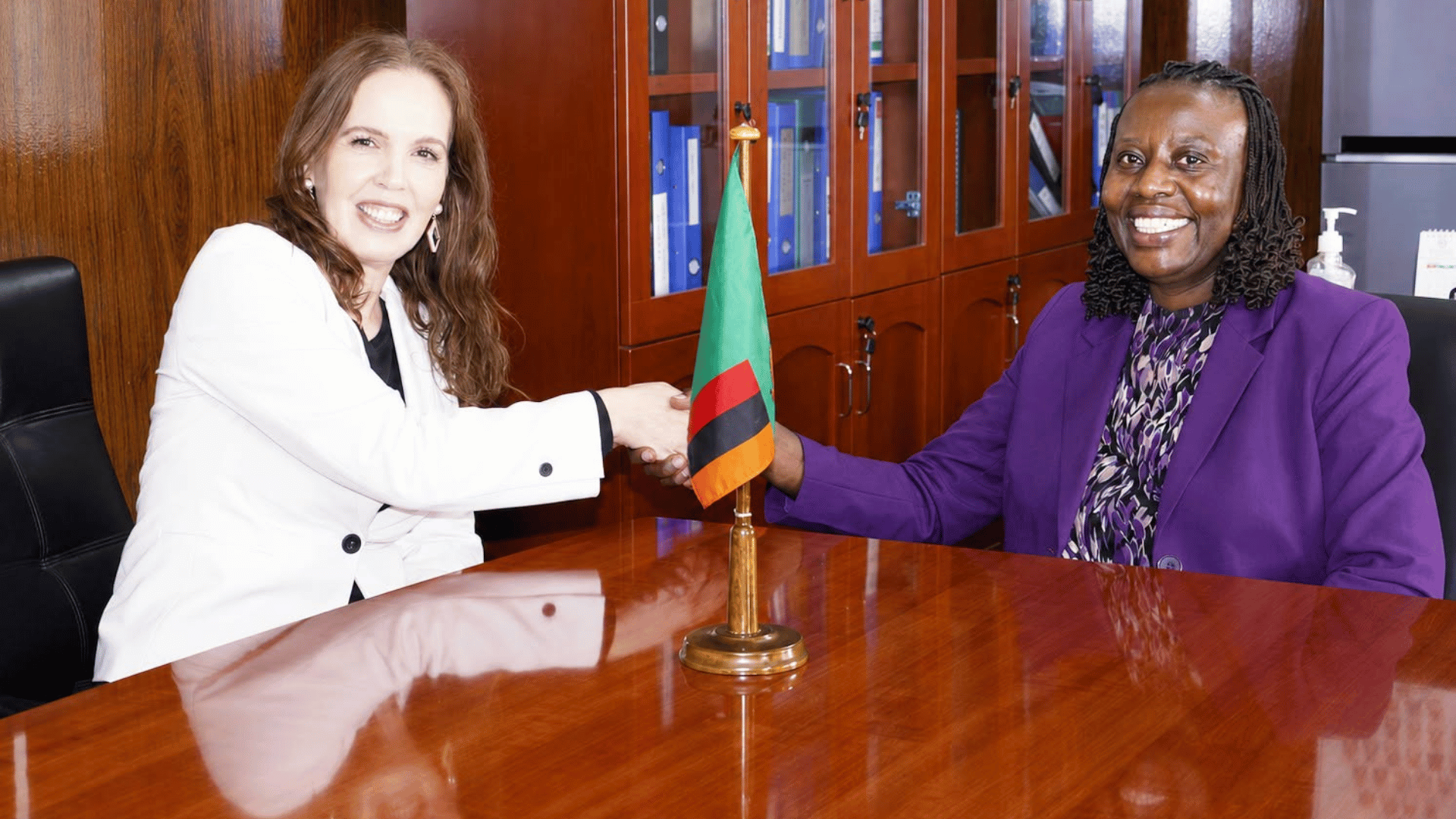 Finland's outgoing Ambassador Saana Halinen shakes hands with Ministry of Finance Permanent Secretary Prudence Kaoma during a farewell courtesy call in Lusaka, with a Zambian flag on the table