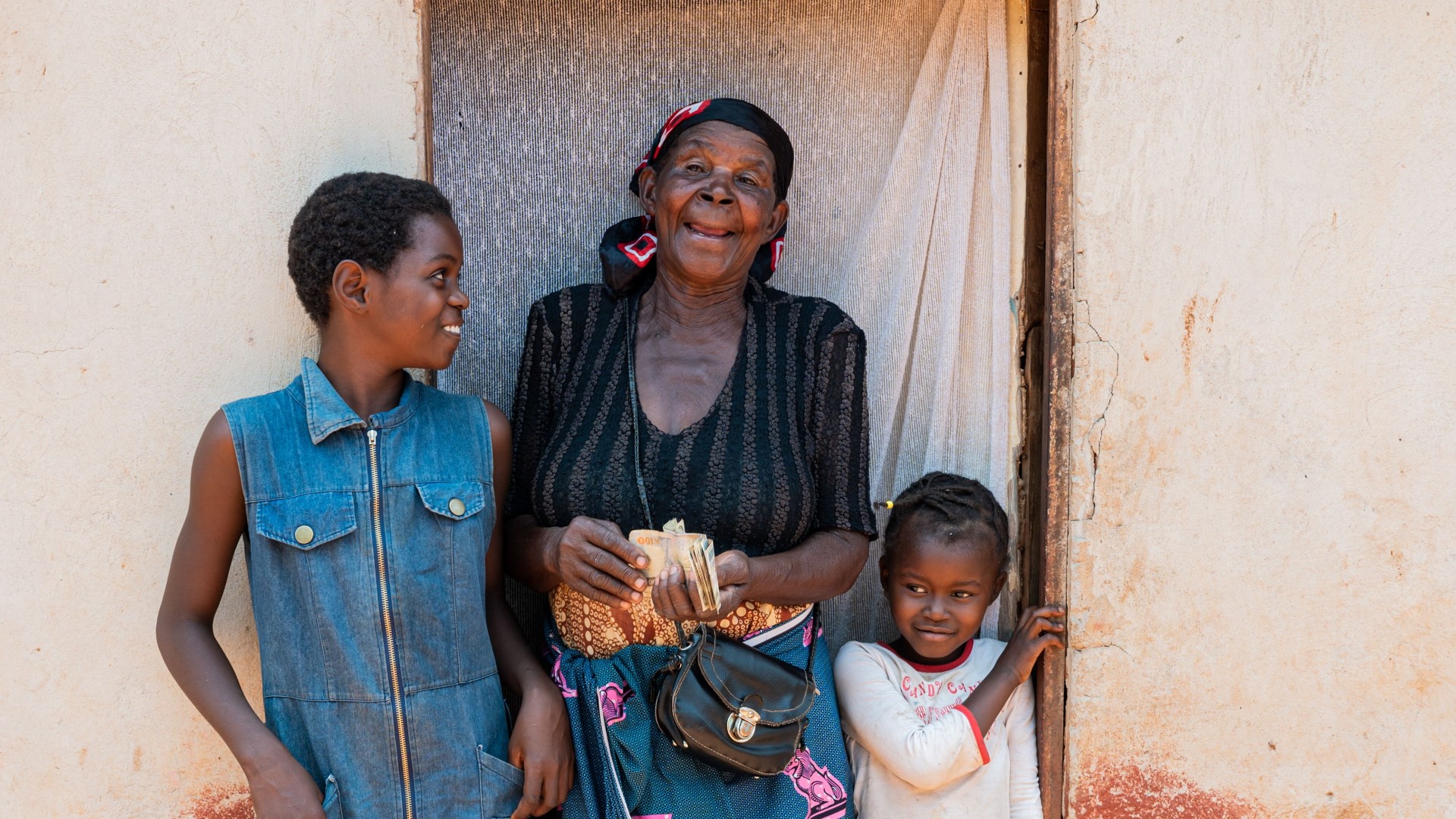 Elderly Zambian woman holding kwacha banknotes received through the Social Cash Transfer Programme