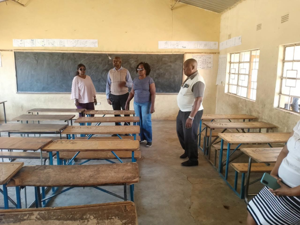 People standing among wooden desks inside a classroom in the photograph supplied with the Mandevu polling-centre inspection update.