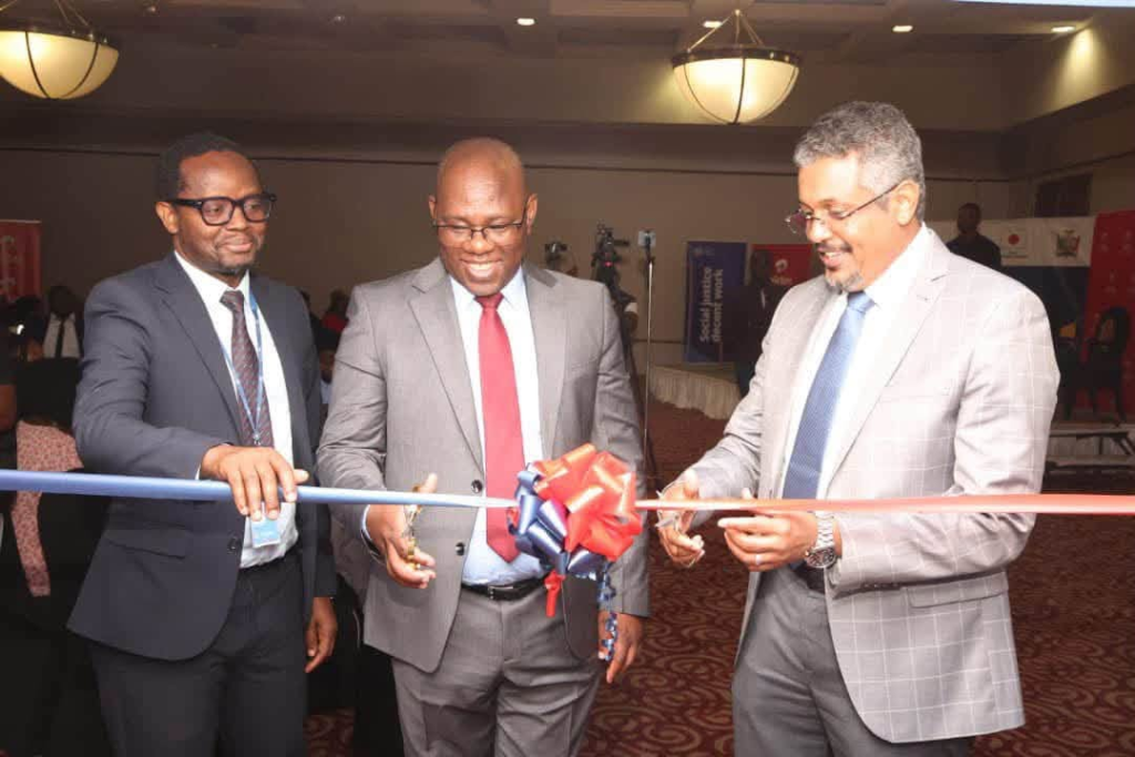 Three men in suits take part in a ribbon-cutting ceremony in the photograph supplied with the Zambia e-waste youth employment briefing.