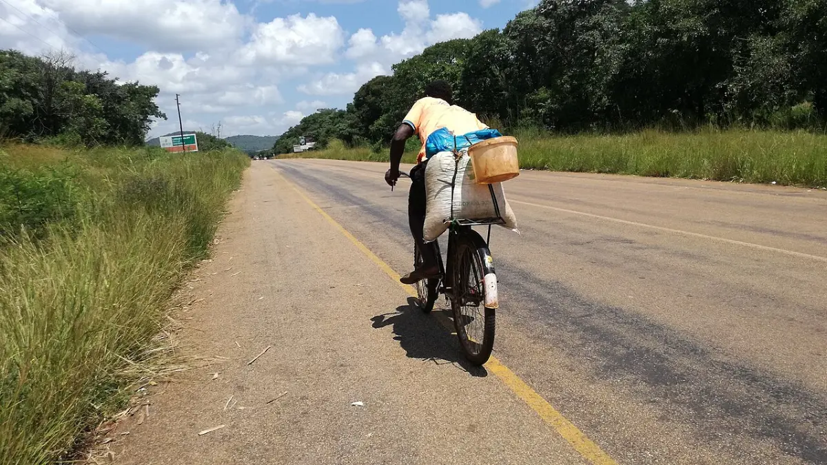 A farmer in Chipata, Zambia, cycles along a highway with a bag of maize strapped to his bicycle.