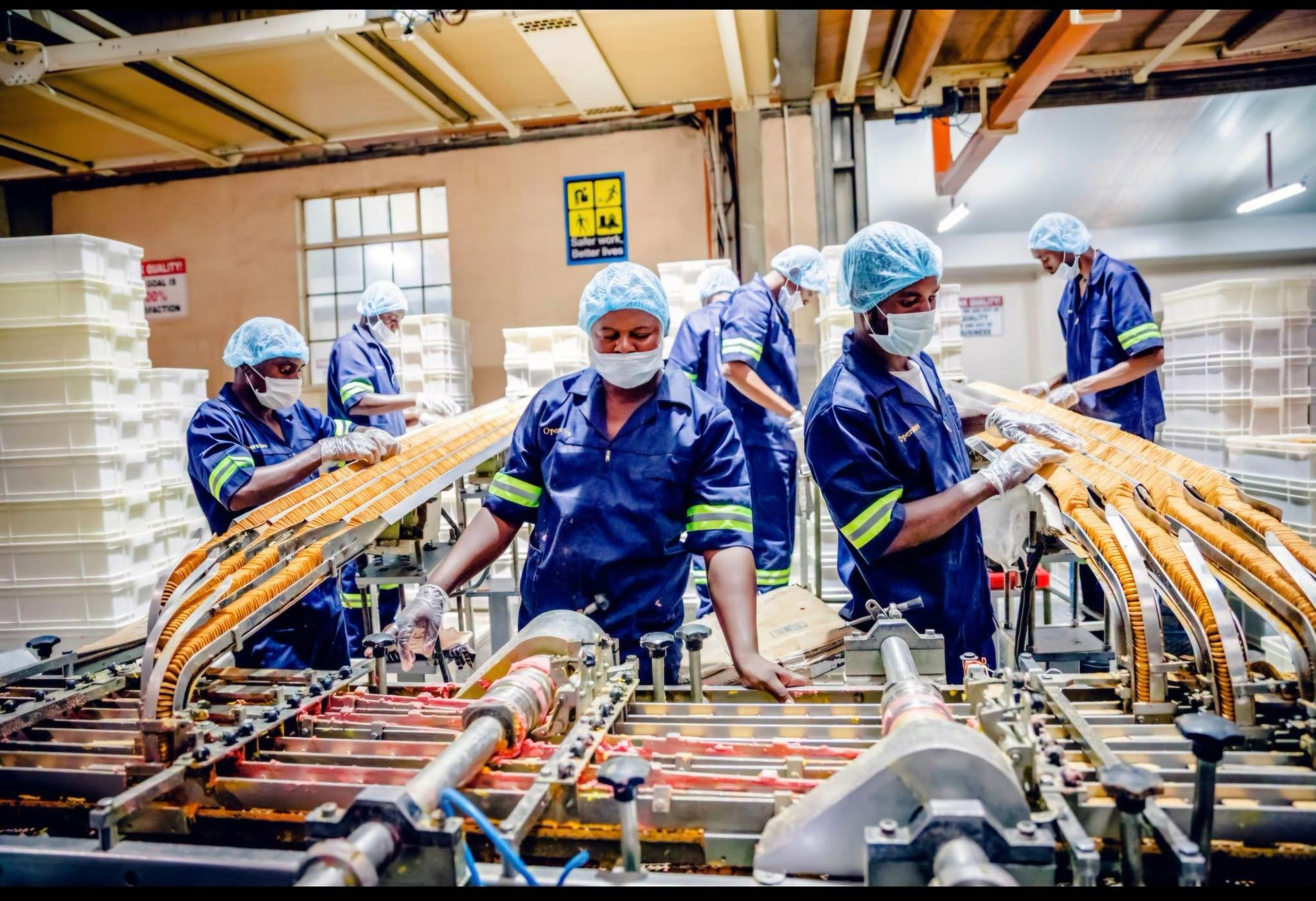 Factory workers in protective clothing inspect products on a manufacturing production line.