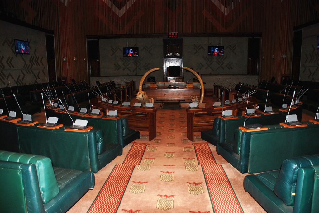 Empty chamber of the National Assembly of Zambia with rows of green leather seats and microphones
