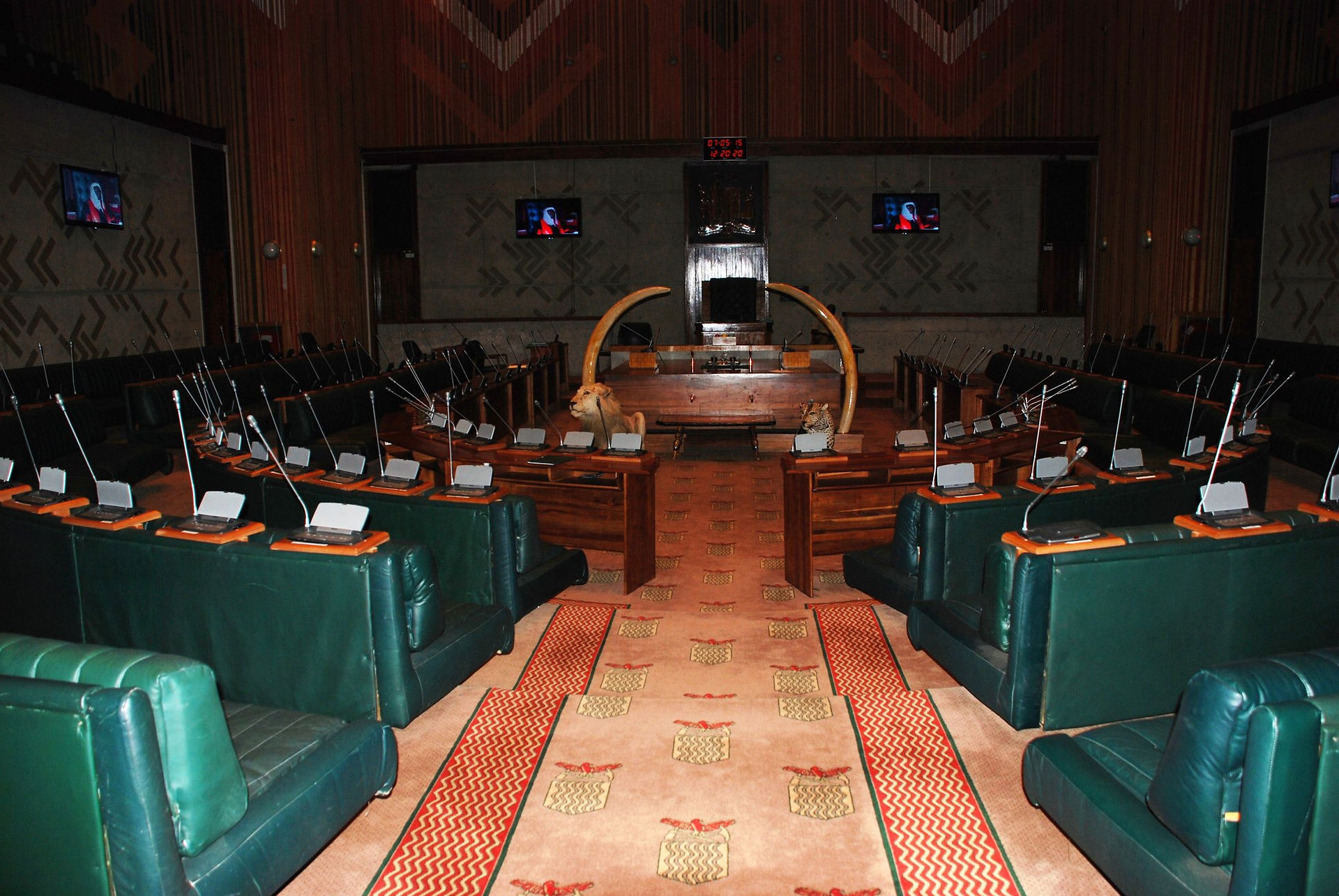 Empty chamber of the National Assembly of Zambia with rows of green leather seats and microphones